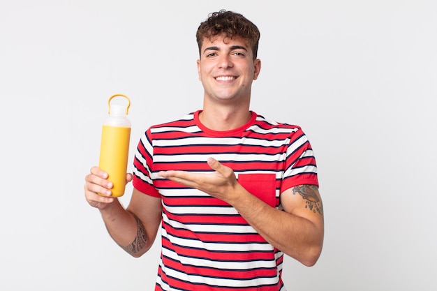 Jeune bel homme souriant gaiement, se sentant heureux et montrant un concept et tenant un thermos de café