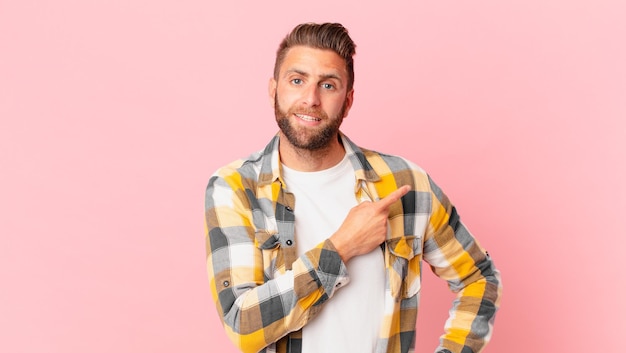 Jeune bel homme souriant gaiement, se sentant heureux et pointant vers le côté