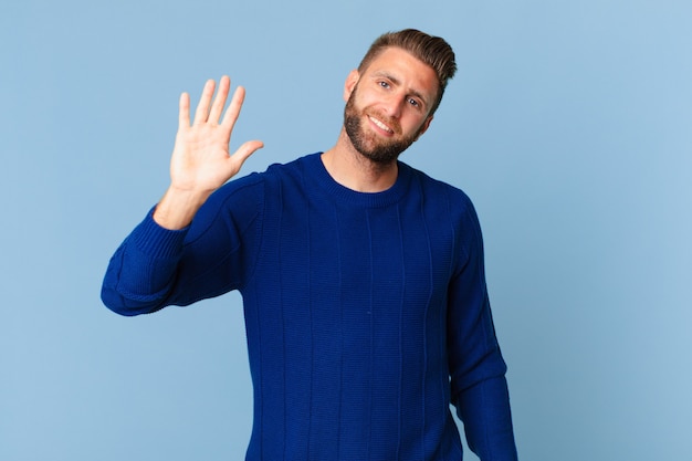 Jeune bel homme souriant joyeusement, agitant la main, vous accueillant et vous saluant