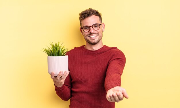 Jeune bel homme souriant joyeusement avec amical et offrant et montrant un concept. concept de plante décorative