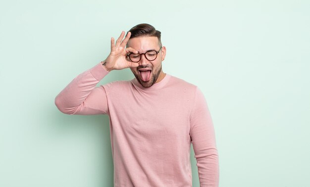 Jeune bel homme souriant joyeusement avec une grimace, plaisantant et regardant à travers le judas, espionnant les secrets