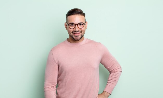 Photo jeune bel homme souriant joyeusement avec une main sur la hanche et une attitude confiante, positive, fière et amicale