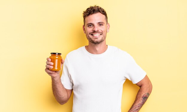 Jeune bel homme souriant joyeusement avec une main sur la hanche et un concept de gelée de pêche confiant