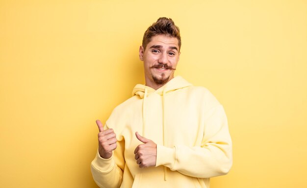 Jeune bel homme souriant joyeusement et nonchalamment pointant vers l'espace de copie sur le côté, se sentant heureux et satisfait. étrange concept de moustache