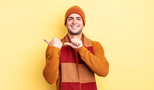 Jeune bel homme souriant joyeusement et nonchalamment pointant vers l'espace de copie sur le côté, se sentant heureux et satisfait