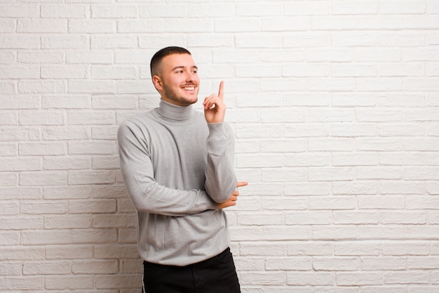 Jeune bel homme souriant joyeusement et regardant de côté, se demandant, pensant ou ayant une idée sur un fond plat