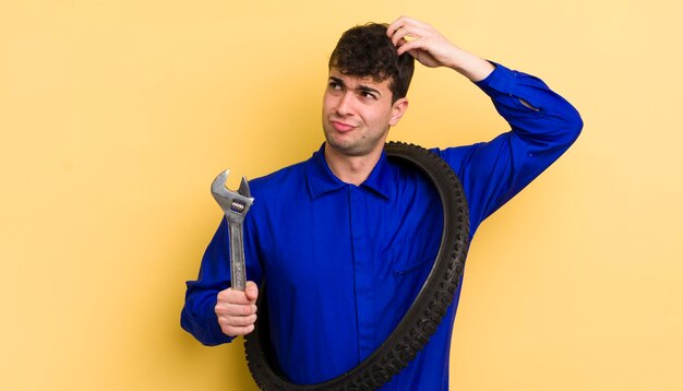 Jeune bel homme souriant joyeusement et rêvassant ou doutant du concept de réparateur de vélo