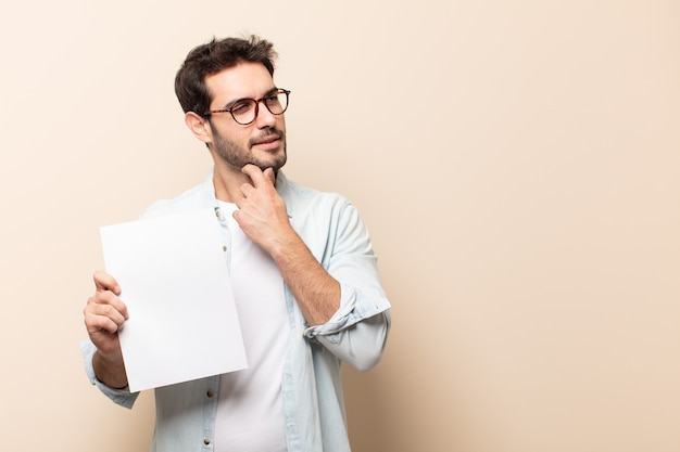 Jeune bel homme souriant joyeusement et rêvassant ou doutant, regardant sur le côté