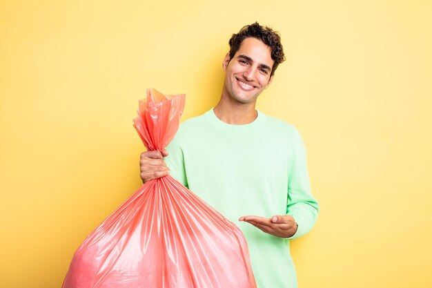 Jeune bel homme souriant joyeusement, se sentant heureux et montrant un concept. concept de sac poubelle