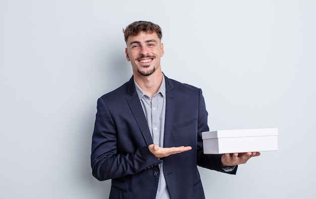 Jeune bel homme souriant joyeusement, se sentant heureux et montrant un concept. paquet de boîte blanche