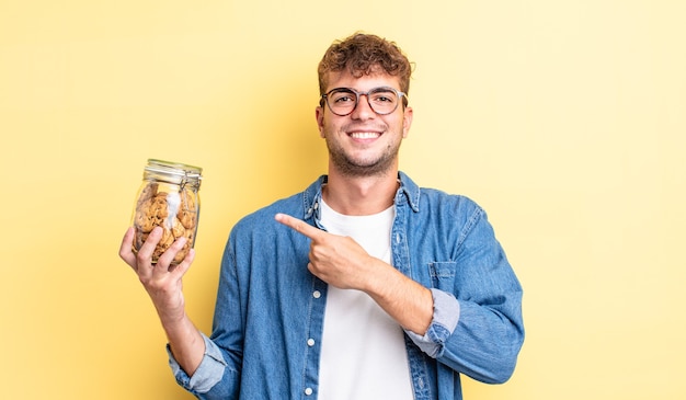 Jeune bel homme souriant joyeusement, se sentant heureux et pointant sur le côté. concept de bouteille de biscuits