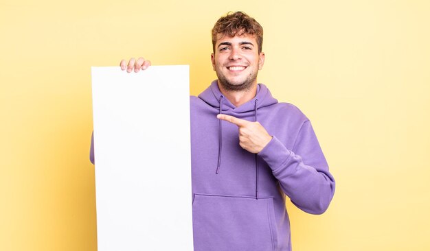 Jeune bel homme souriant joyeusement, se sentant heureux et pointant sur le côté. concept d'espace de copie