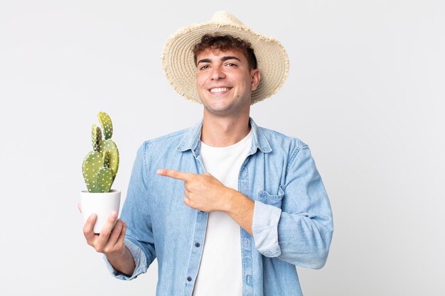 Jeune bel homme souriant joyeusement, se sentant heureux et pointant sur le côté. fermier tenant un cactus décoratif