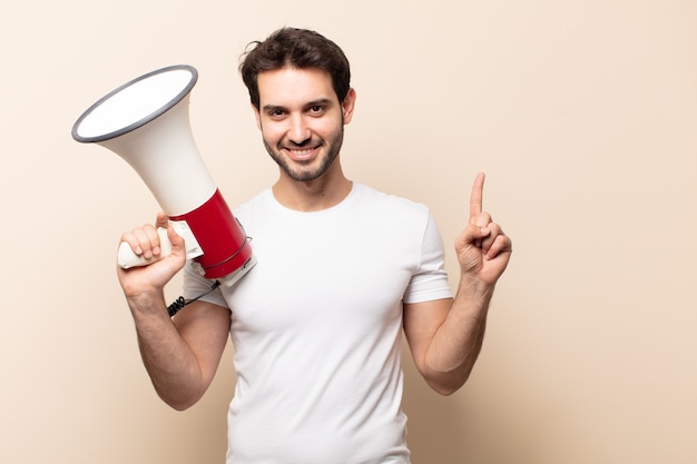 Jeune bel homme souriant joyeusement, se sentant heureux et pointant vers le côté et vers le haut, montrant l'objet dans l'espace de copie