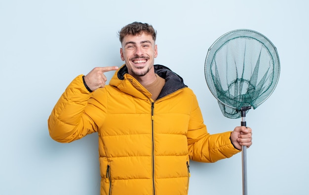 Jeune bel homme souriant pointant avec confiance vers son propre large sourire. concept de pêcheur