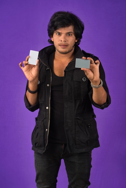 Jeune bel homme souriant posant avec une carte de crédit sur fond violet