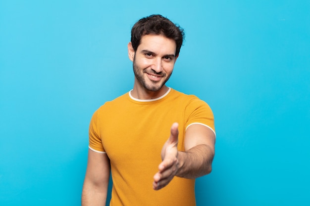 Jeune bel homme souriant, à la recherche de plaisir, confiant et sympathique, offrant une poignée de main pour conclure un accord, coopérant