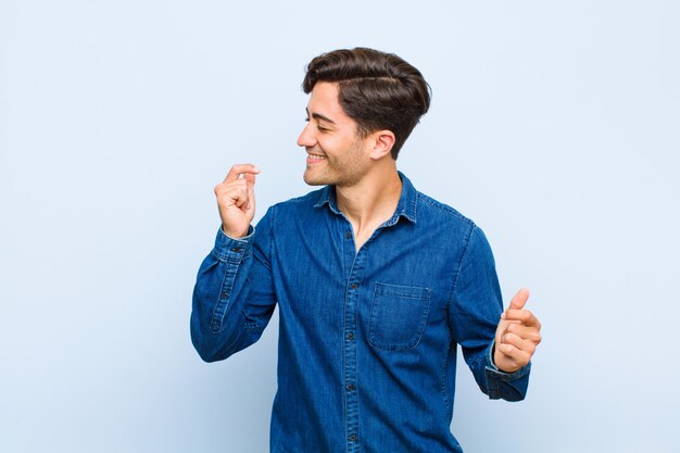 Jeune bel homme souriant, se sentant insouciant, détendu et heureux, dansant et écoutant de la musique, s'amusant lors d'une fête contre le mur bleu