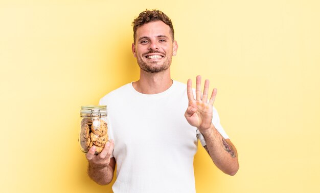 Jeune bel homme souriant et semblant amical, montrant le concept de bouteille de biscuits numéro quatre