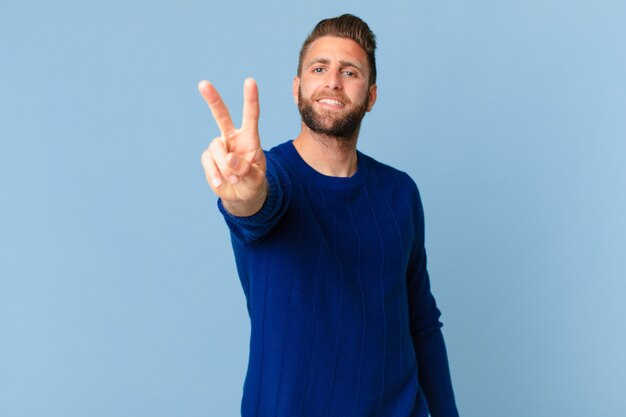 Jeune bel homme souriant et semblant heureux, gesticulant la victoire ou la paix