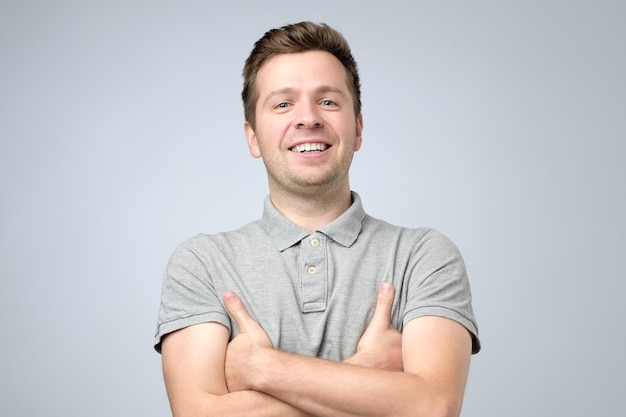 Jeune bel homme souriant en t-shirt debout avec les mains croisées