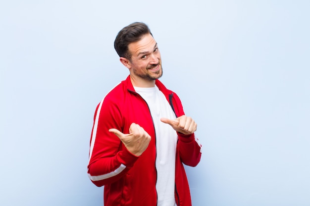 Jeune bel homme sportif ou moniteur souriant, gaiement et désinvolte, pointant du côté de la surface, se sentant heureux et satisfait contre le mur plat