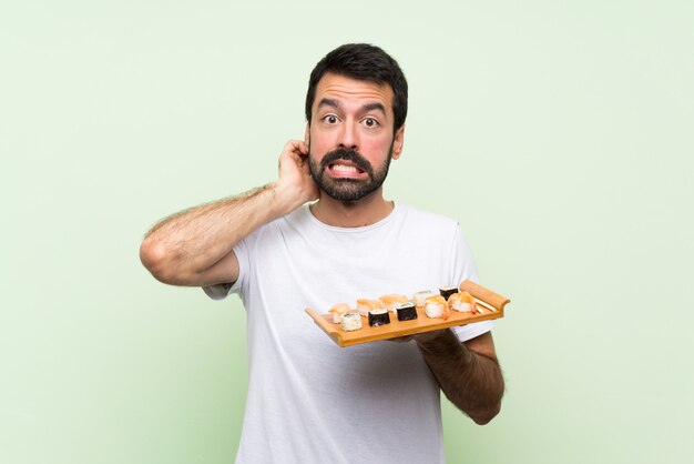 Jeune bel homme avec sushi sur mur vert isolé ayant des doutes