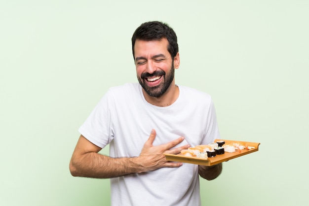 Jeune bel homme avec sushi sur mur vert isolé souriant beaucoup