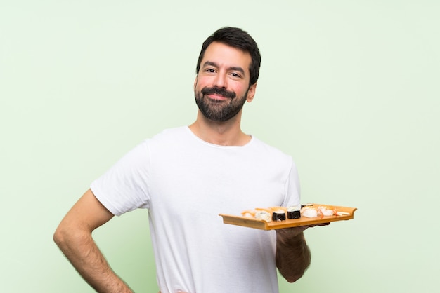 Jeune bel homme avec sushi posant avec les bras à la hanche et souriant