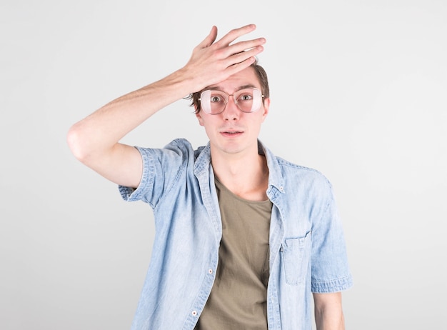 Jeune bel homme en t-shirt décontracté, debout contre un mur blanc, embarrassé et interrogé. Incertain de doute, réfléchissant, posant sa main sur sa tête. Concept réfléchi.