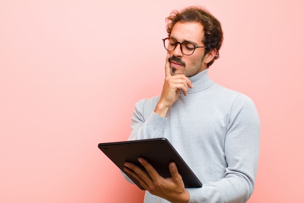 Jeune bel homme avec une tablette contre un mur plat rose