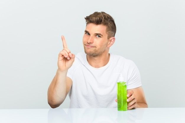 Jeune bel homme tenant une bouteille d'aloe vera montrant le numéro un avec le doigt.