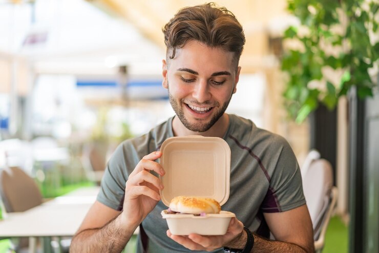 Photo jeune bel homme tenant un hamburger avec une expression heureuse