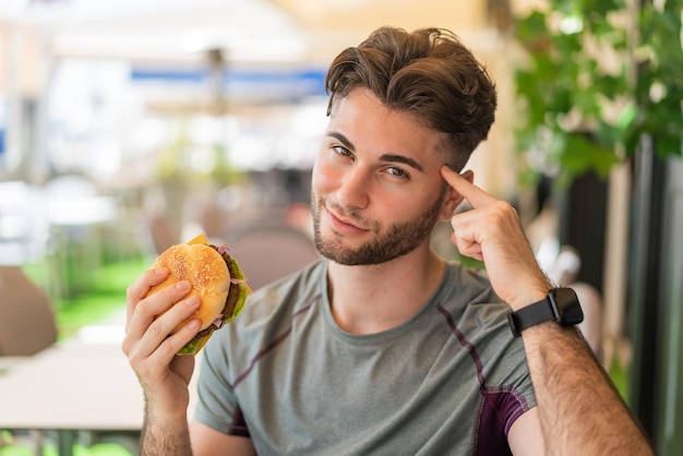 Jeune bel homme tenant un hamburger et pensant