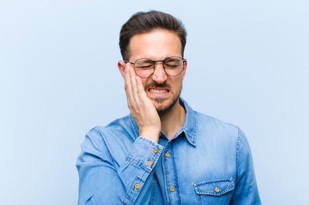 Jeune bel homme tenant la joue et souffrant de maux de dents douloureux, se sentant mal, misérable et malheureux, à la recherche d'un dentiste