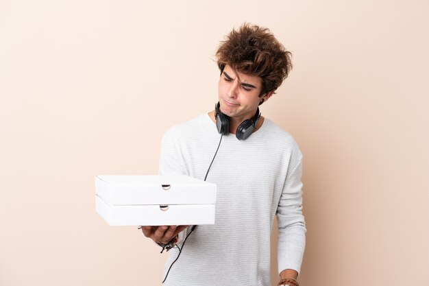 Jeune bel homme tenant une pizza sur un mur isolé avec une expression triste