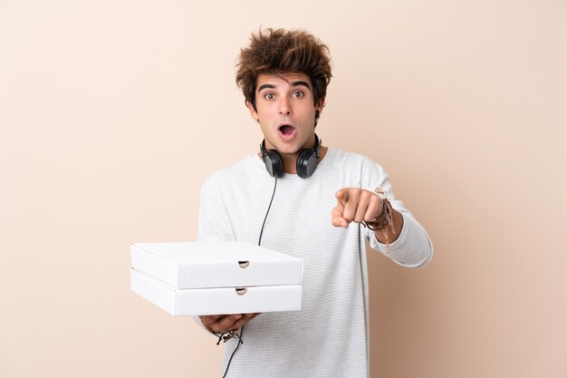 Jeune bel homme tenant une pizza sur un mur isolé surpris et pointant vers l'avant