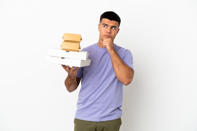 Jeune bel homme tenant des pizzas et des hamburgers sur fond blanc isolé et levant