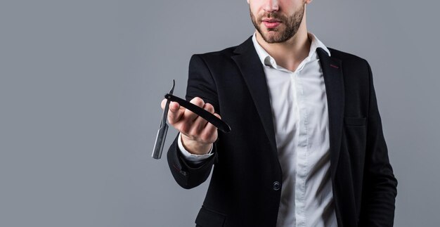 Jeune bel homme en tenue de soirée a des poils sur le visage tenir un salon de coiffure à lame de rasoir