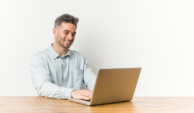 Jeune bel homme travaillant avec son ordinateur portable souriant confiant avec les bras croisés