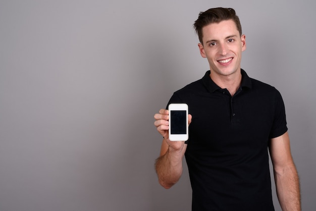 jeune bel homme utilisant un téléphone portable sur fond gris