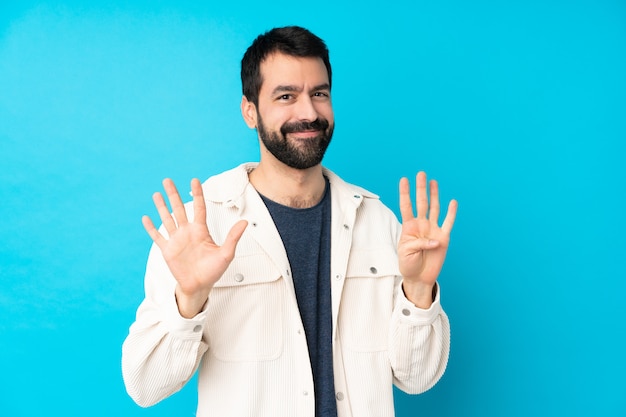Jeune bel homme avec veste en velours côtelé blanc sur mur bleu isolé comptant neuf avec les doigts