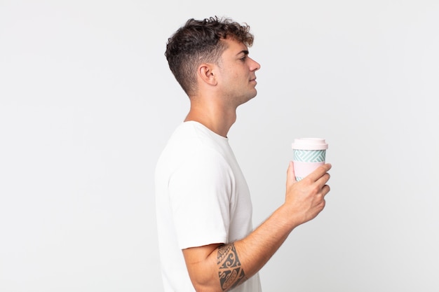 Jeune bel homme sur la vue de profil pensant, imaginant ou rêvant et tenant un café à emporter