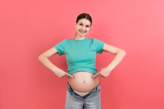 Jeune belle adolescente enceinte attendant bébé sur fond coloré isolé souriant montrant gros ventre