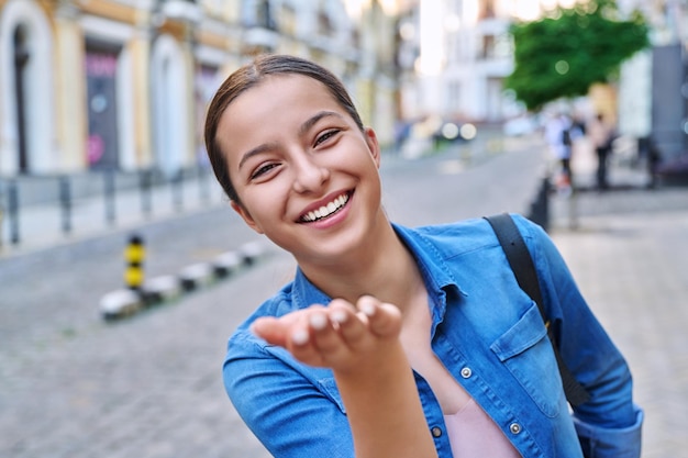 Jeune belle adolescente heureuse montrant un baiser aérien avec sa main dans la rue de la ville
