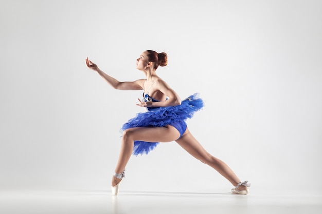 Jeune belle ballerine avec chignon recueilli des cheveux portant une robe bleue et des chaussons de pointe dansant gracieusement isolé sur fond blanc. intérieur, tourné en studio.