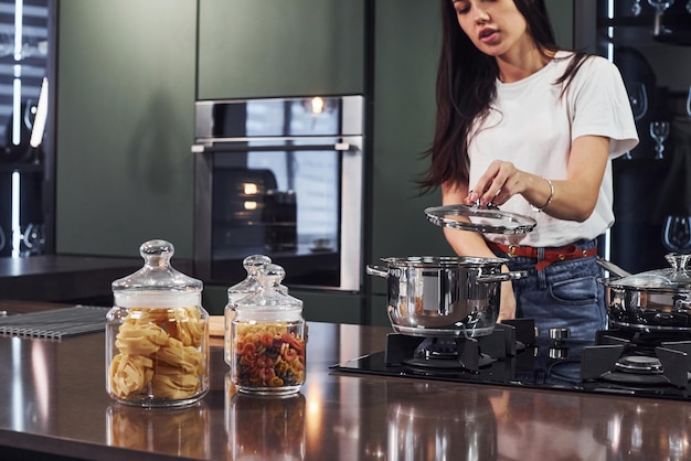 Jeune belle brune en vêtements décontractés préparant des aliments sains dans la cuisine pendant la journée