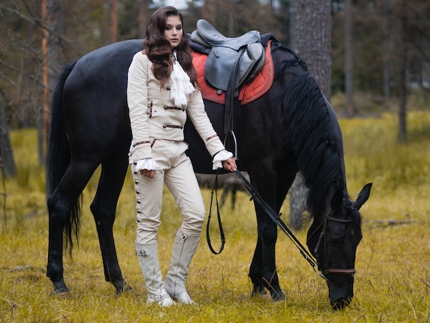 Une jeune belle cavalière brune à côté d'un cheval noir en pleine munition