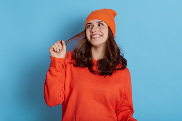 Jeune belle dame regarde rêveusement de côté, souriant joyeusement isolé sur bleu, tirant ses cheveux sur le côté