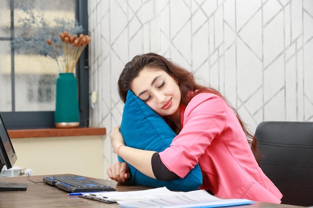 Jeune belle dame tenant étreint son oreiller et s'endormir au bureau